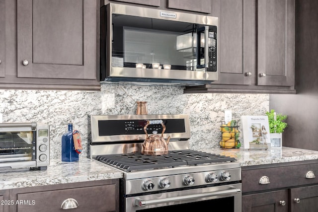 kitchen featuring stainless steel appliances, dark brown cabinetry, tasteful backsplash, and light stone countertops