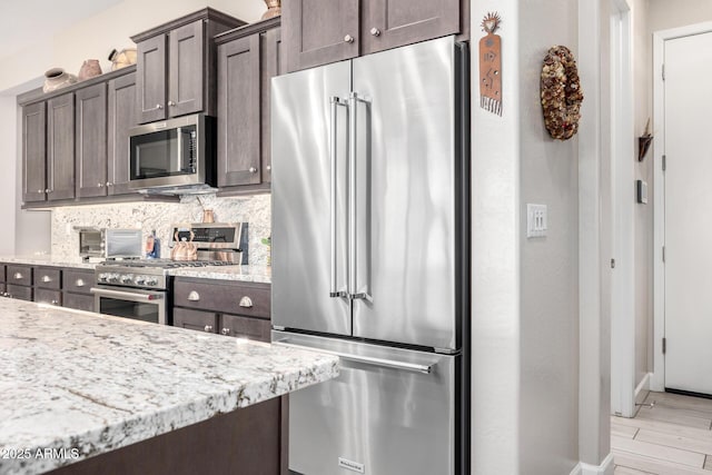 kitchen featuring high end appliances, dark brown cabinets, tasteful backsplash, baseboards, and light stone counters