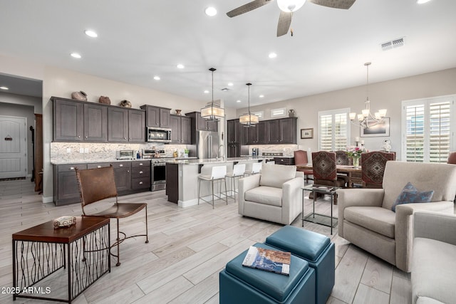 living room with a chandelier, ceiling fan, recessed lighting, and light wood finished floors