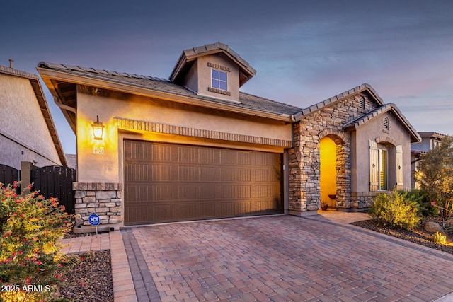 view of front of property featuring stone siding, stucco siding, a garage, and decorative driveway