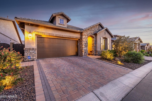 view of front of home featuring stone siding, a garage, decorative driveway, and stucco siding