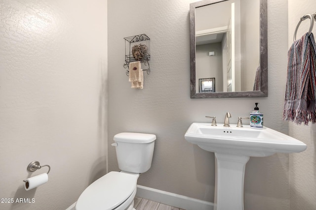 bathroom featuring toilet, baseboards, a sink, and wood finished floors
