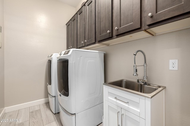 laundry area featuring washing machine and dryer, cabinet space, baseboards, and light wood-style flooring