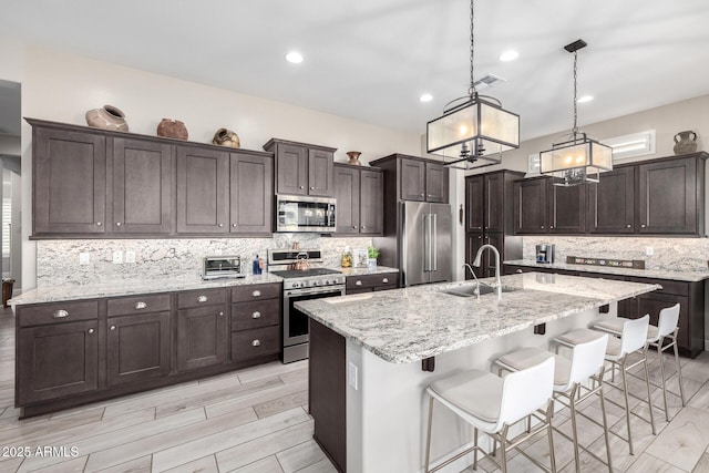kitchen with stainless steel appliances, a sink, a chandelier, dark brown cabinetry, and backsplash