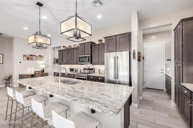 kitchen featuring premium appliances, a sink, dark brown cabinets, a chandelier, and tasteful backsplash