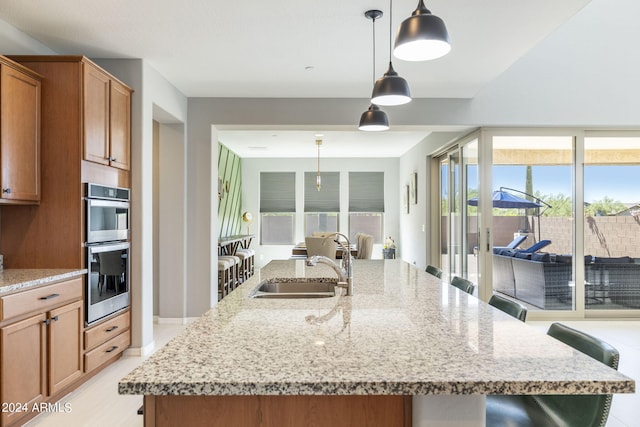 kitchen featuring a kitchen breakfast bar, pendant lighting, double oven, and a kitchen island with sink