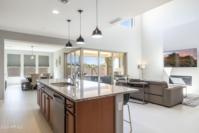 kitchen with a kitchen island with sink, dishwasher, light stone countertops, pendant lighting, and sink