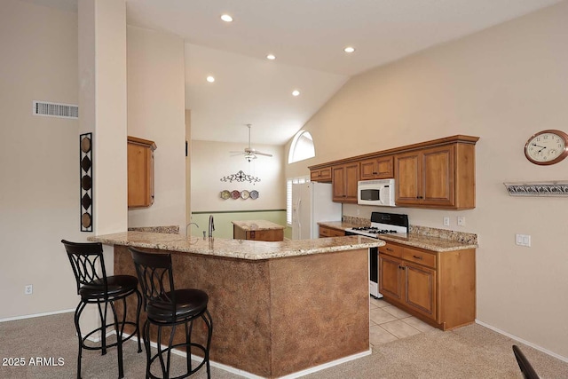 4081 N 156th Dr, Goodyear, AZ 85395 - kitchen featuring white appliances, light carpet, brown cabinetry, a peninsula, and a breakfast bar
