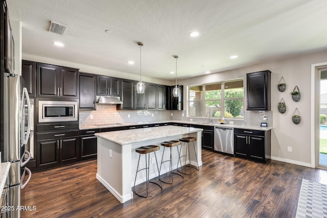 11875 W Lone Tree Trl, Peoria, AZ 85383 - kitchen featuring appliances with stainless steel finishes, under cabinet range hood, a kitchen island, dark wood finished floors, and tasteful backsplash