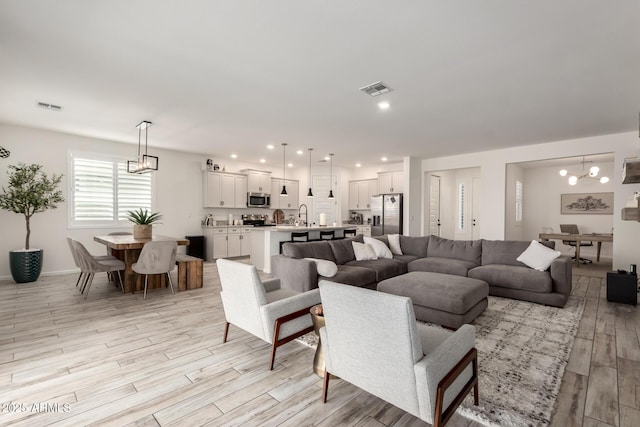 living room featuring light wood-style floors, baseboards, visible vents, and a chandelier