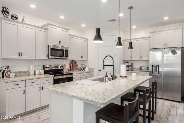 kitchen featuring appliances with stainless steel finishes, a breakfast bar, a sink, an island with sink, and visible vents