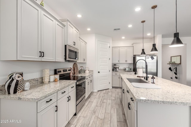 kitchen featuring visible vents, a kitchen island with sink, light wood finished floors, decorative light fixtures, and stainless steel appliances