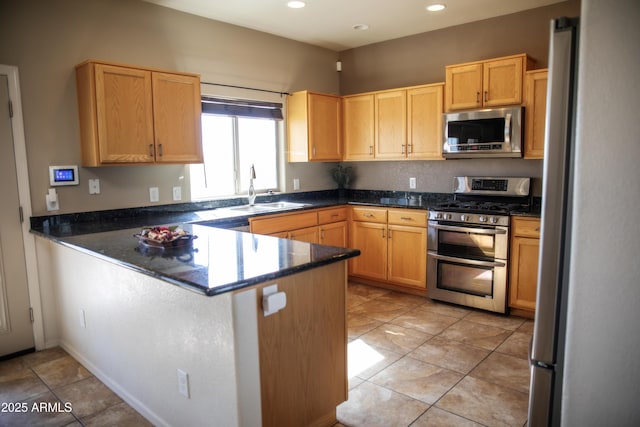 kitchen with light tile patterned flooring, appliances with stainless steel finishes, sink, dark stone countertops, and kitchen peninsula