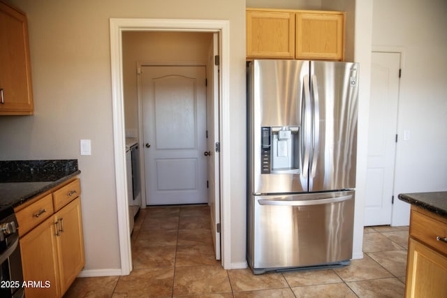 kitchen featuring light tile patterned floors, dark stone counters, stainless steel fridge with ice dispenser, and stove