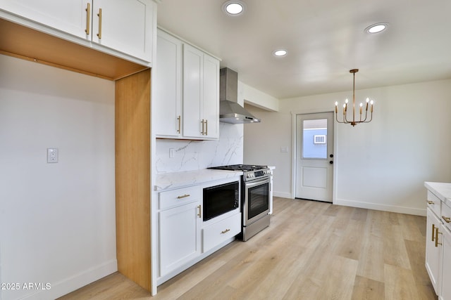 kitchen with wall chimney exhaust hood, stainless steel gas range, light stone countertops, and white cabinets