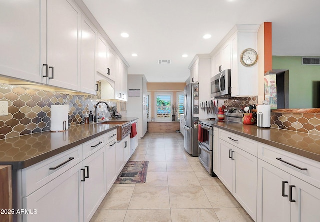 kitchen with decorative backsplash, white cabinets, appliances with stainless steel finishes, and light tile patterned flooring