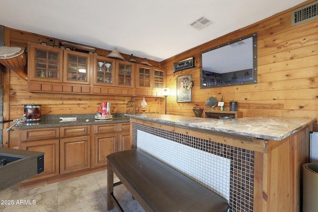 bar with light tile patterned floors, wood walls, and stone countertops