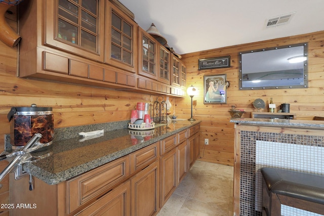 bar with light tile patterned floors, dark stone counters, and wooden walls