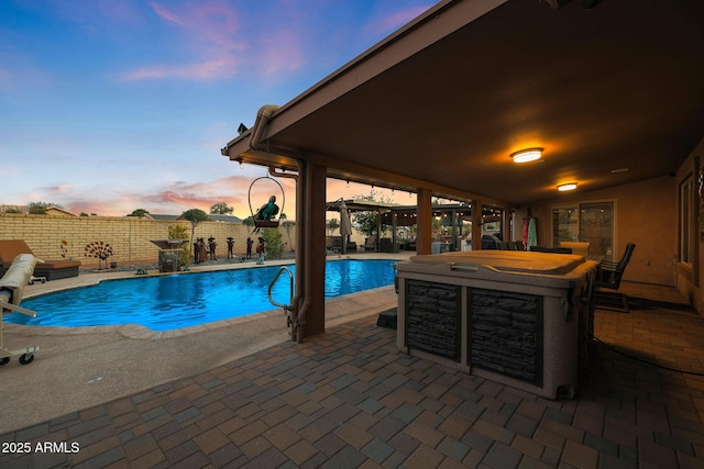 pool at dusk with a patio area and a hot tub