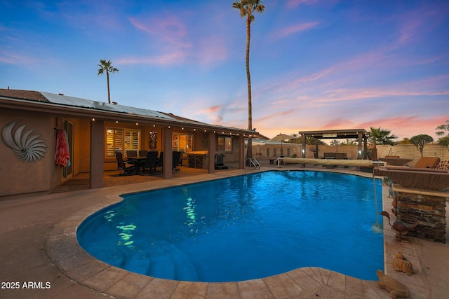 pool at dusk featuring pool water feature and a patio