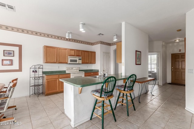 kitchen with a kitchen breakfast bar, light tile patterned flooring, white appliances, and sink