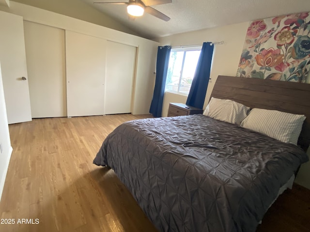 bedroom with light wood-style floors, lofted ceiling, a closet, and ceiling fan