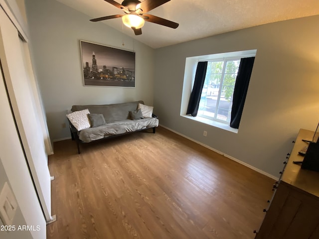 living area featuring wood finished floors, ceiling fan, baseboards, and lofted ceiling
