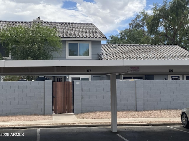 view of front facade featuring a tiled roof, a fenced front yard, covered parking, and a gate