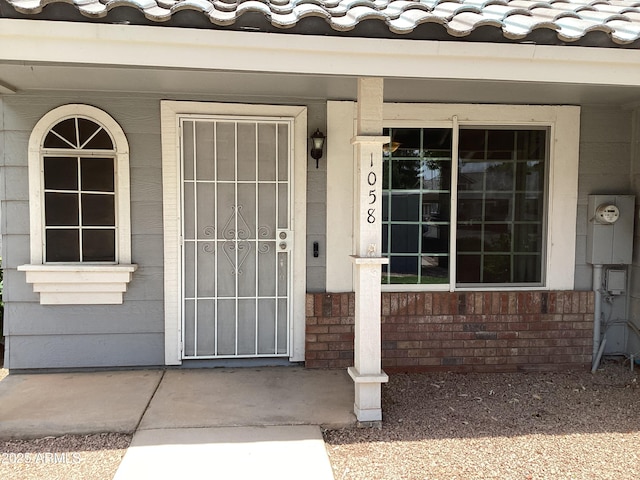 view of exterior entry featuring a porch and a tiled roof