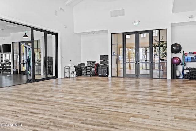 gym with a high ceiling, light wood-type flooring, and french doors