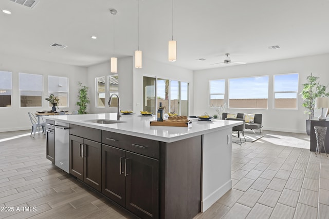 kitchen featuring pendant lighting, sink, ceiling fan, dark brown cabinets, and a center island with sink