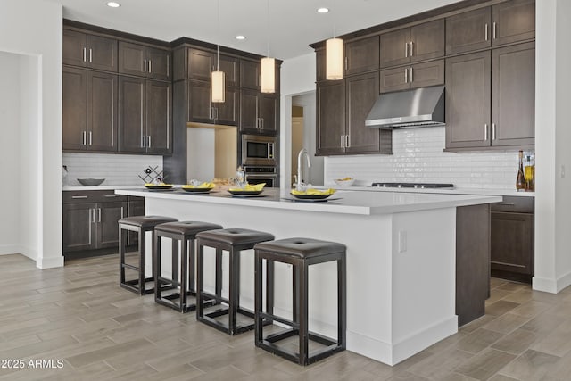 kitchen featuring a breakfast bar, appliances with stainless steel finishes, dark brown cabinetry, a center island with sink, and decorative light fixtures