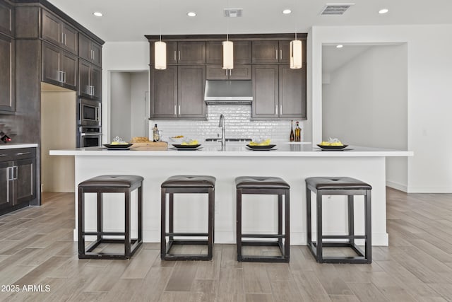 kitchen featuring appliances with stainless steel finishes, a kitchen breakfast bar, a kitchen island with sink, and hanging light fixtures