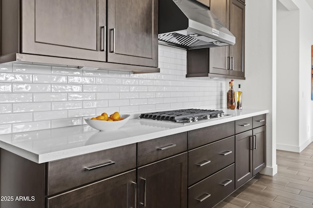 kitchen with dark wood-type flooring, range hood, dark brown cabinetry, decorative backsplash, and stainless steel gas stovetop