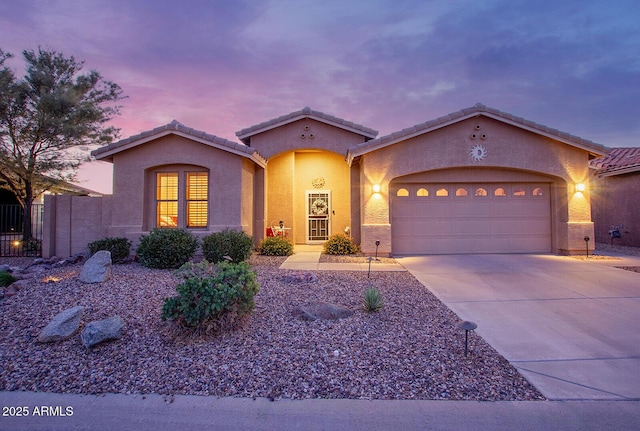 mediterranean / spanish home featuring concrete driveway, a garage, stucco siding, a tiled roof, and fence
