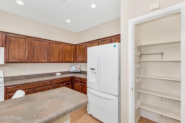 kitchen featuring white refrigerator with ice dispenser, light tile patterned flooring, recessed lighting, and brown cabinets
