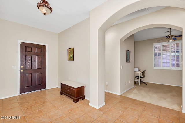 foyer entrance featuring ceiling fan, light tile patterned flooring, arched walkways, and baseboards