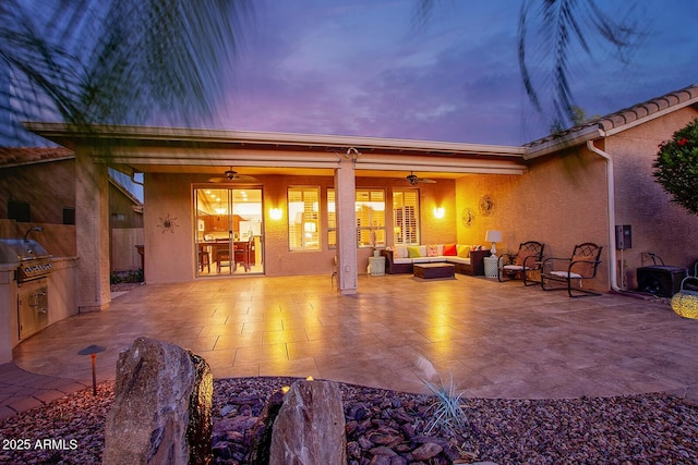 rear view of property with an outdoor living space with a fire pit, exterior kitchen, stucco siding, a patio area, and a ceiling fan