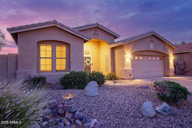 mediterranean / spanish-style home featuring a garage, stucco siding, concrete driveway, and a tiled roof