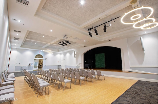 cinema with wood finished floors, arched walkways, coffered ceiling, a raised ceiling, and rail lighting