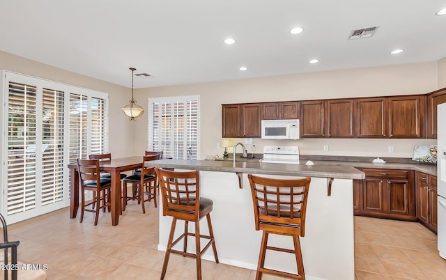 kitchen with white microwave, stove, light tile patterned floors, a kitchen bar, and a sink