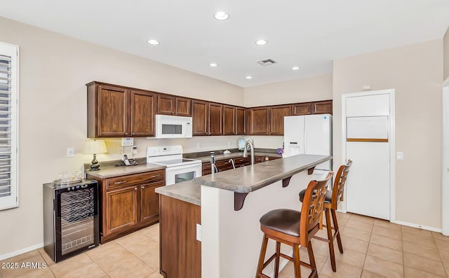 kitchen with white appliances, light tile patterned flooring, beverage cooler, a breakfast bar area, and recessed lighting