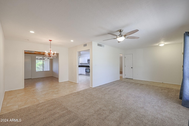 carpeted spare room featuring ceiling fan with notable chandelier and a textured ceiling