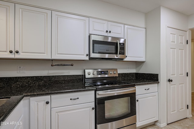 kitchen with white cabinets, light tile patterned flooring, dark stone countertops, and appliances with stainless steel finishes