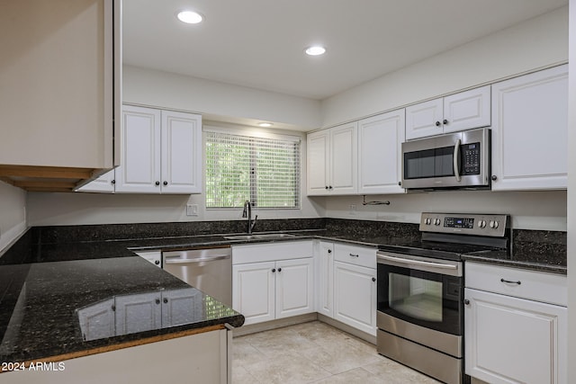 kitchen with stainless steel appliances, white cabinets, sink, light tile patterned flooring, and dark stone countertops