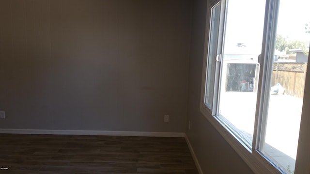 empty room featuring dark wood-style flooring, plenty of natural light, and baseboards