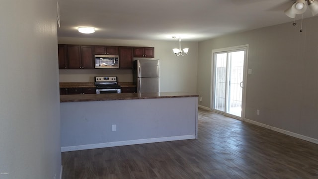 kitchen featuring stainless steel appliances, a chandelier, dark wood finished floors, a peninsula, and baseboards