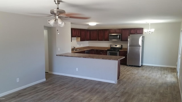 kitchen featuring stainless steel appliances, a peninsula, wood finished floors, and baseboards