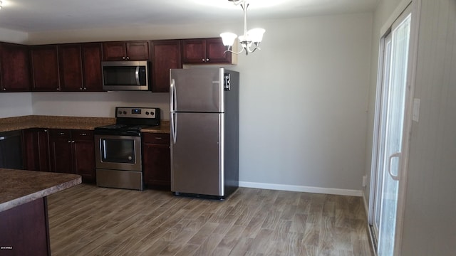 kitchen with stainless steel appliances, a chandelier, light wood-style floors, baseboards, and decorative light fixtures