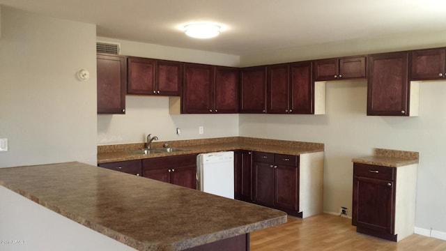 kitchen featuring dishwasher, a sink, a peninsula, light wood-style flooring, and dark countertops